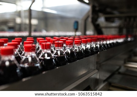 Bottling factory - Black juice or soft drink bottling line for processing and bottling juice into bottles. Selective focus.  Royalty-Free Stock Photo #1063515842