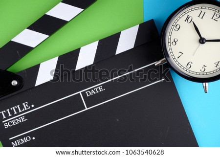 movie time. clapper board and alarm clock over blue and green paper