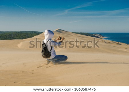 tourist in the desert. girl traveler takes pictures of desert sands on a mobile phone. Woman tourist in a white jacket walking on sand. wind in the desert. Pilat Dune 