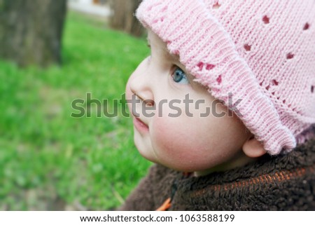 baby in a plush sweater, playing on a warm spring day, on a bright green grass. the infant is sitting on the green grass. baby plays .baby is looking up, against the background of green grass