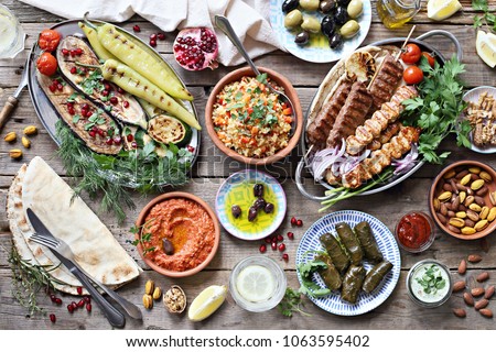Middle eastern, arabic or mediterranean dinner table with grilled lamb kebab, chicken skewers  with roasted vegetables and appetizers variety serving on rustic outdoor table. Overhead view. Royalty-Free Stock Photo #1063595402