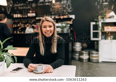 Portrait of a young blonde woman having a cup of coffee at the modern cafe.