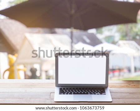 Modern laptop on wooden table blurred garden at restaurant background.