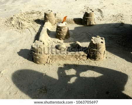 A sand castle at a beach with a shadow of a person with a love sign