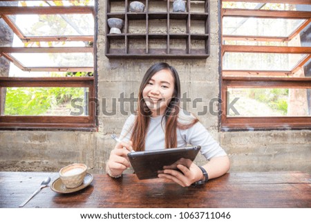 Attractive smiling young asian business women holding digital tablet information searching on wood in cafe