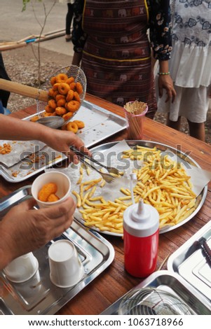 Fresh fried yummy potato chips and fish nuggets just out from the fryer on tray.Kids wating for their que to get some.Paper cups,red ketchup bottle and many cooking tool in picture.