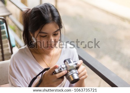 Pretty cool young Asian woman checking photo on the mirrorless camera or retro film camera in the coffee cafe