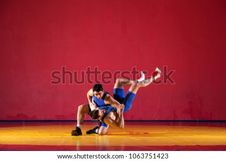 Two strong wrestlers in blue  wrestling tights are wrestlng and making a  making a hip throw  on a yellow wrestling carpet in the gym. Young man doing grapple.
