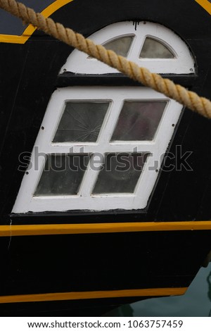 Close up view of an oblique white painted window located in a black wooden vessel. Rope in front of the ancient boat. Graphic design with lines and curves. Abstract maritime image of an old ship.