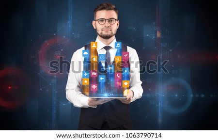 Elegant businessman holding tablet with hologram application icons and symbols above