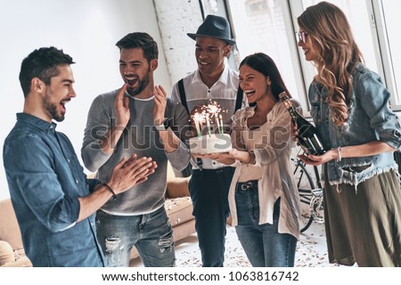 Make a wish! Happy young man celebrating birthday among friends while standing in room with confetti on the floor