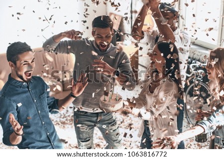 Best birthday party! Top view of happy young man celebrating birthday among friends while standing in room with confetti flying around