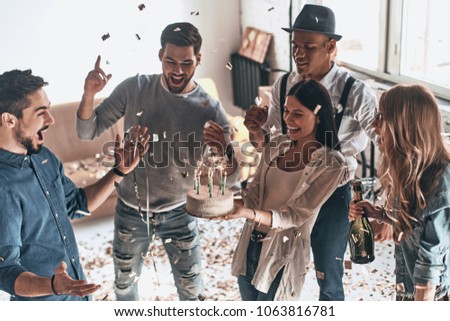 Time for a birthday cake. Top view of happy young man celebrating birthday among friends while standing in room with confetti flying around