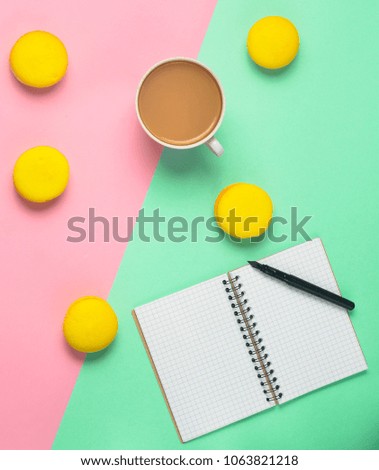 Notebook with a pen, a cup of coffee and yellow macaroons on a pastel colored background. Trend of minimalism. Top view. Flat lay.