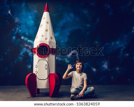 Boy is sitting near toy rocket on space background and waving hand.