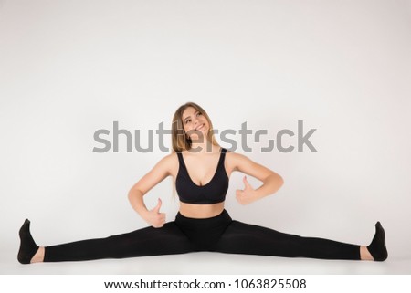 Young sports girl with a nice body sitting on a twine. Performs gymnastic exercises. Good smiles. Shows with fingers like.