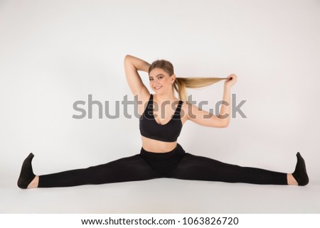 Young sports girl with a nice body sitting on a twine. Performs gymnastic exercises. Good smiles. Hold hands with her hair.