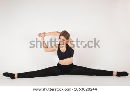 Young sports girl with a nice body sitting on a twine. Performs gymnastic exercises. Good smiles. Dressed in sportswear.