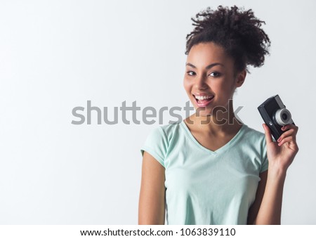 Cheerful Afro-American girl in casual clothes is holding a photo camera and smiling, isolated on white