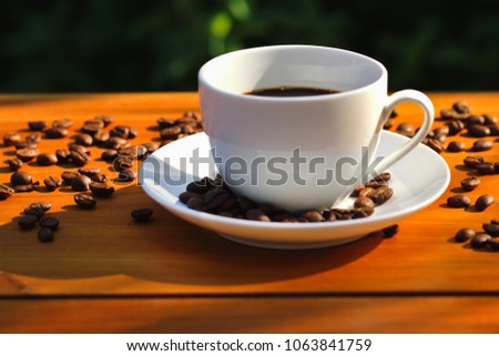 Cup of coffee on wooden table with morning light and blurred nature background.