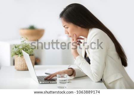 Puzzled confused asian woman thinking hard concerned about online problem solution looking at laptop screen, worried serious korean businesswoman focused on solving difficult work computer task Royalty-Free Stock Photo #1063889174