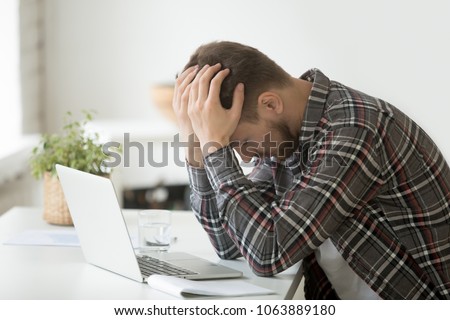 Frustrated depressed man holding head in hands shocked by bankruptcy stock downfall sitting at work desk with laptop, stressed tired businessman feels despair lost money online or got problem debt Royalty-Free Stock Photo #1063889180