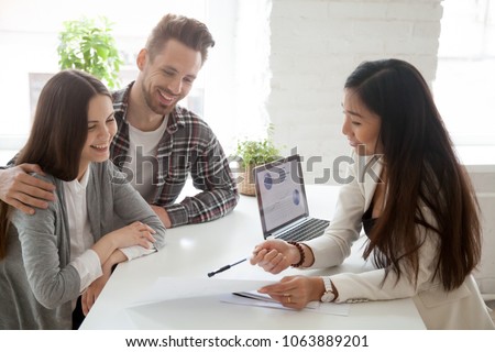 Asian woman realtor, insurance broker or financial advisor consulting young millennial couple clients customers about buying renting house or mortgage loan investment showing contract at meeting Royalty-Free Stock Photo #1063889201