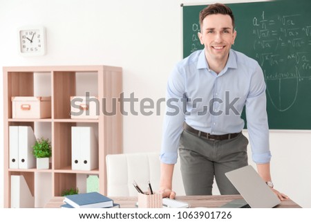 Young male teacher standing near table in classroom