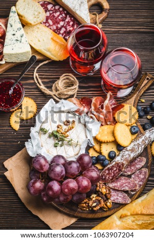 Close-up of wooden boards with cold meat, variety of cheese, fruit, bread and glasses of red wine. Wooden background. Delicatessen plate. Mix of different snacks/appetizers. Close-up. Delicacy platter
