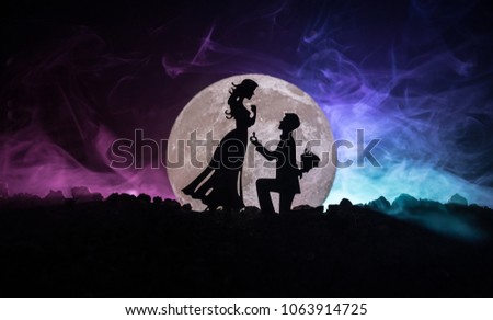 Amazing love scene. Silhouettes of man making proposal to woman or Silhouettes of couple against big moon at background. Selective focus