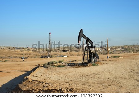 An oil well pumps crude out of the Kern County (California) fields while a servicing rig works in the background