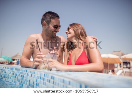 Happy young couple relaxing and drink cocktails in the swimming pool.