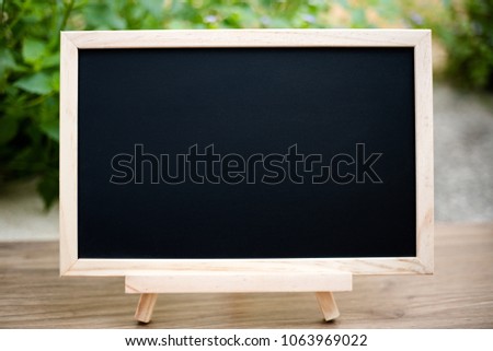 Black board on wood table top with sun and blur green tree bokeh background, Template mock up for display of product