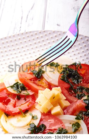 A beautiful spring salad from tomatoes, onions, cheese and green dressing. Eating on a large elegant plate. Unusual iridescent cutlery. Delicious and easy food for a healthy diet from a nutritionist.
