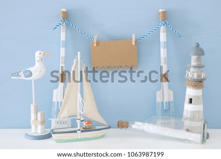 nautical concept with hanging empty note on a string next to lighthouse, boat, letter in the bottle and seagull over blue background