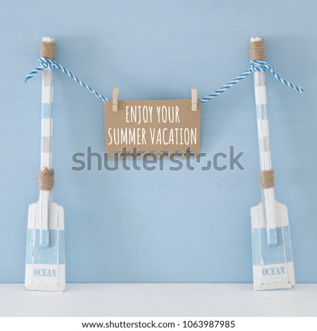 nautical concept with wooden decorative boat oars and note hanging on a string over blue background