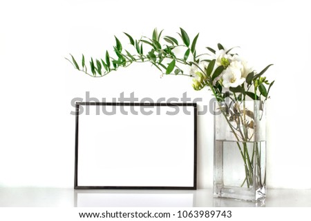 Green branches in a vase with a frame for presentation of works and text. Everything is on the table in the interior.Mock-up for displaying works.