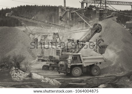 Excavator loads gravel in the dump-body truck against the background of a gravel plant, sepia. Mining industry. Mine and quarry equipment.