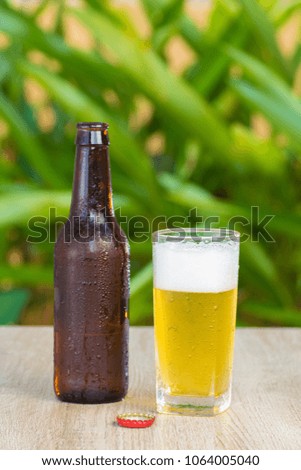 Brown Beer bottles and a glass filled with beer with foam on a table on a green background