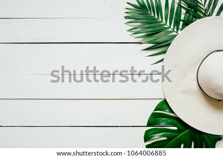 White straw hat, green plam leaves on wooden baclground. Summer holidays vacation concept. Poster banner, postcard template. Royalty-Free Stock Photo #1064006885