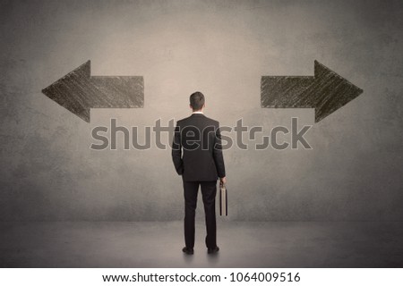 Business man taking a decision while standing in front of two grungy arrows on wall concept
