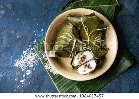 Asian rice piramidal steamed dumplings from rice tapioca flour with meat filling in banana leaves served in ceramic bowl with rice above over blue texture background. Top view, space.