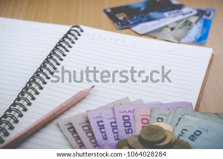 Make a note of your credit card spending. Helps to manage money smoothly, preventing interest from credit cards unnecessarily. In the picture there are notebooks, pencils, credit cards and cash.