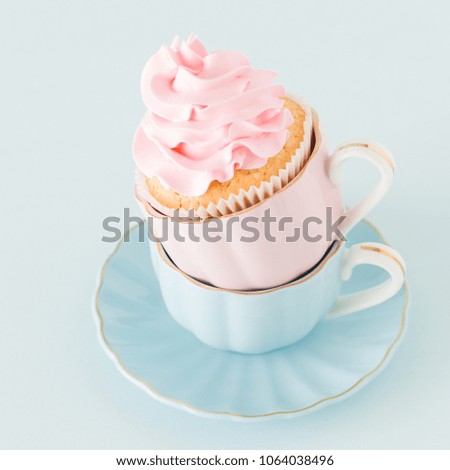 Cupcake with gentle pink cream decoration in two cups on blue pastel background - congratulation card for birthday or valentine day.