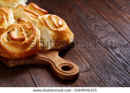 Homemade rose buns on wooden cutting board over rustic vintage background, close-up, shallow depth of field