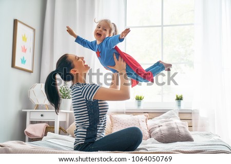 Mother and her child playing together. Girl and mom in Superhero costume. Mum and kid having fun, smiling and hugging. Family holiday and togetherness. Royalty-Free Stock Photo #1064050769