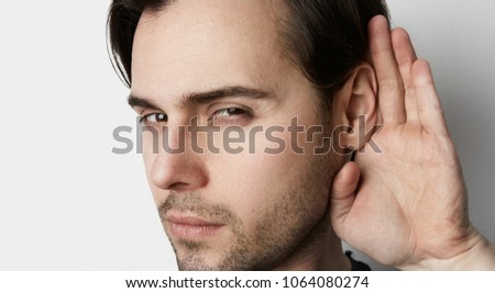 Handsome young man trying to listen to the conversation of someone