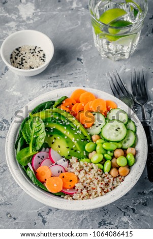 Vegan Buddha bowl salad with spinach, quinoa, chickpeas, avocado, edamame beans, cucumbers, carrots, radish and sesame seeds. Top view