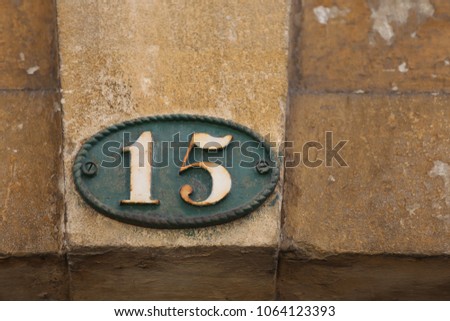 Close up outdoor view of the number fifteen written in white on an oval metallic plate. 
