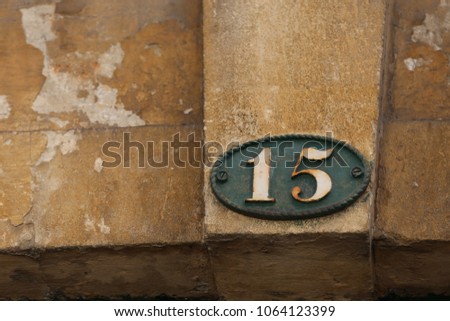 Close up outdoor view of the number fifteen written in white on an oval metallic plate.